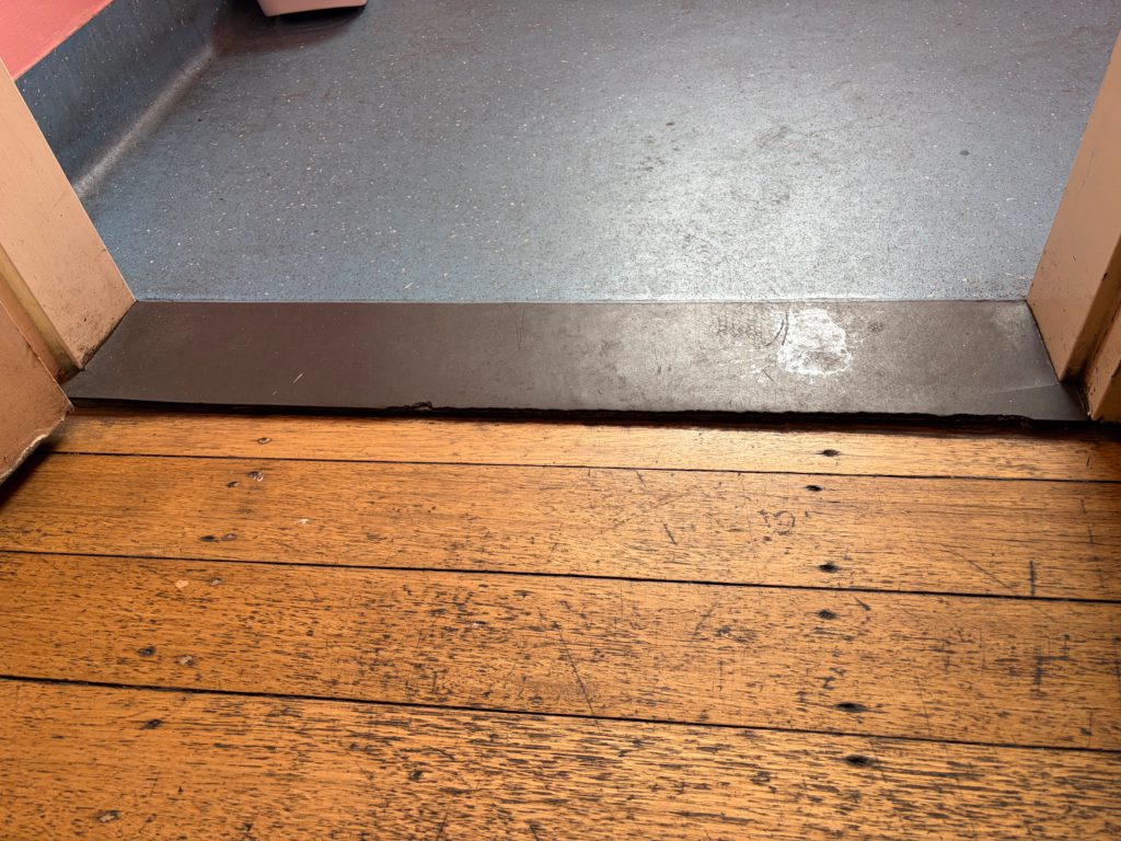 Close-up of the small lip at the accessible toilet doorway, included to show the floor transition.